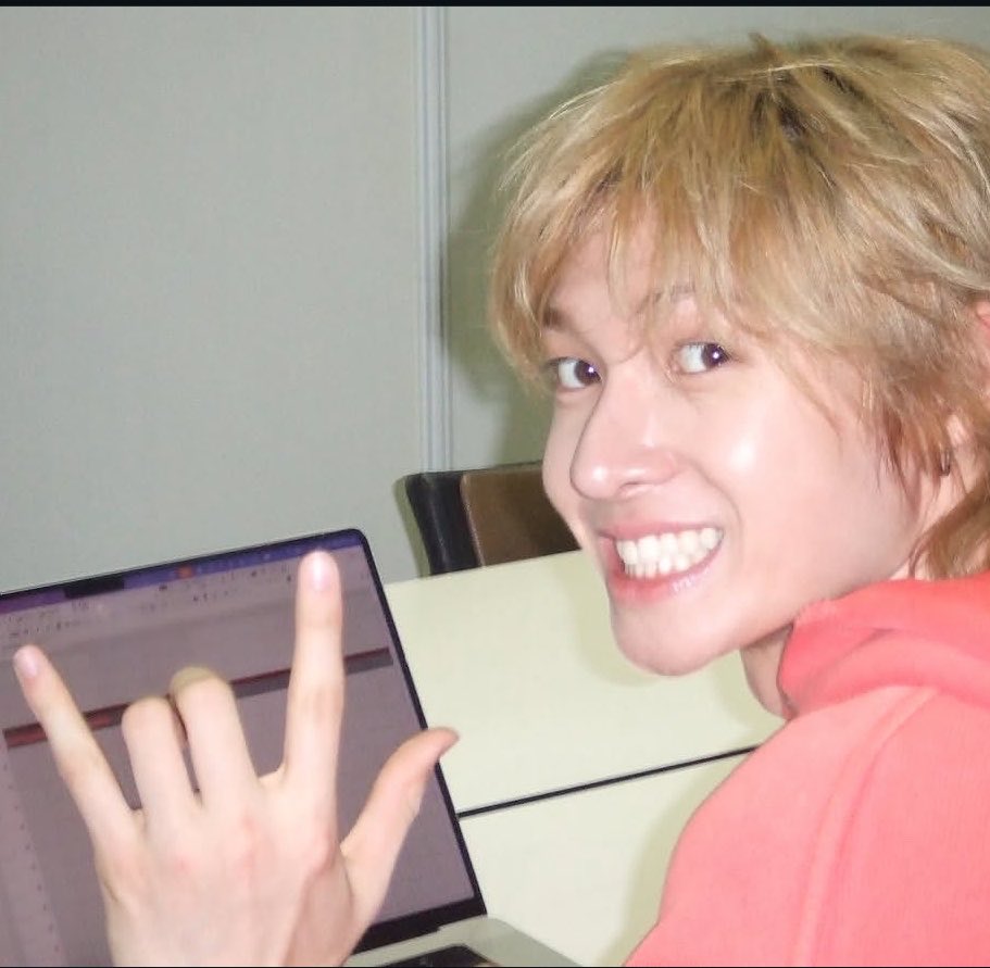 A flash photo of Martin of CORTIS smiling over a laptop, shot on a digital compact camera