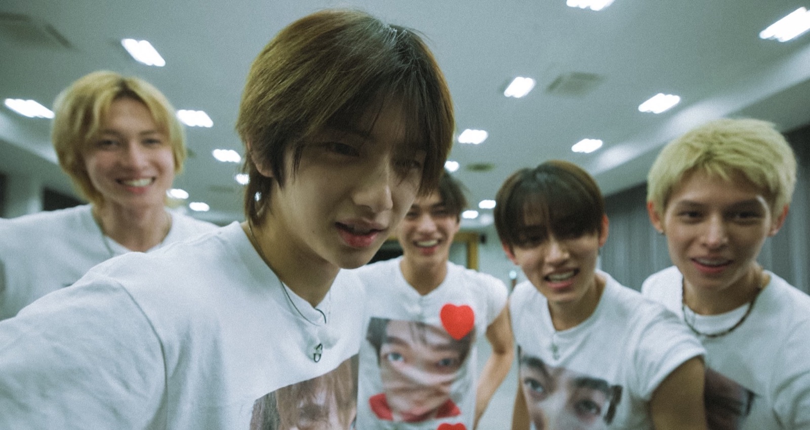 The five members of CORTIS in white t-shirts, laughing into the camera