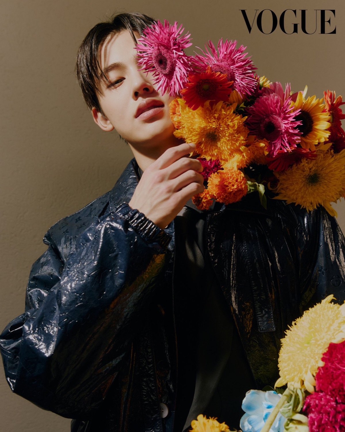Seonghyeon of CORTIS in a navy Louis Vuitton monogram jacket with an armful of pink and orange gerberas