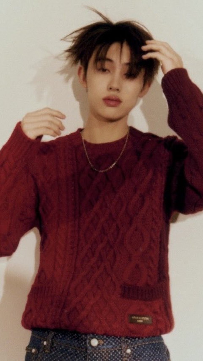 Seonghyeon of CORTIS pushing his hair back, wearing a red Louis Vuitton cable knit and denim