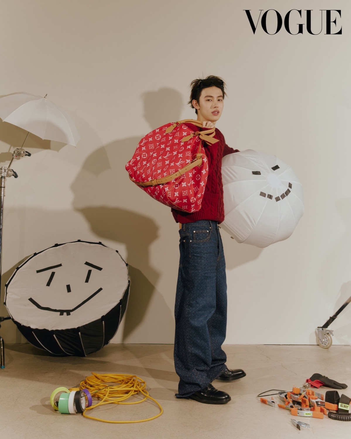 Seonghyeon of CORTIS in a red Louis Vuitton cable knit carrying a red monogram Speedy bag and a studio umbrella