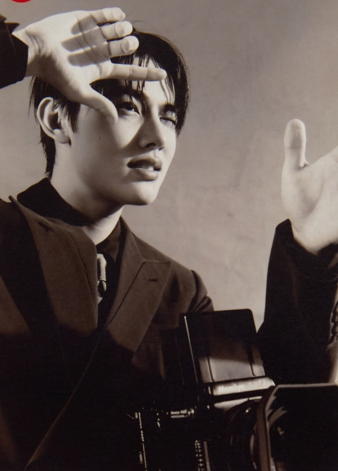 Seonghyeon of CORTIS framing a shot with his hands next to a Mamiya medium format camera, in a brown suit