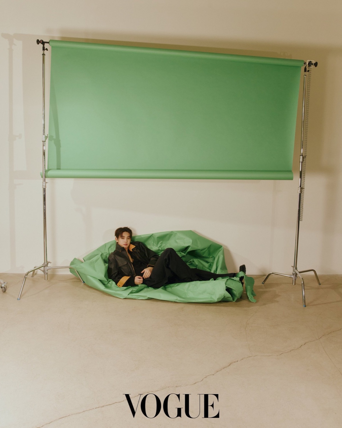 Seonghyeon of CORTIS lying on a collapsed green paper backdrop in a black leather jacket