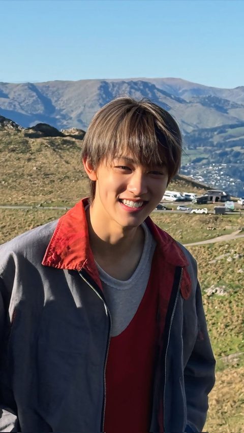 CORTIS Seonghyeon phone wallpaper, smiling in a red collared jacket in the mountains